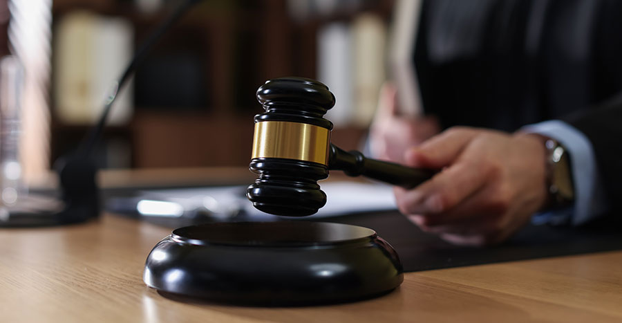 Судья ударом молотка за деревянным столом в помещении